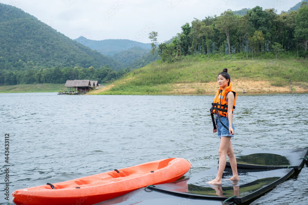 Asian girls in orange life jacket with the backdrop of water and mountains Ready for travel as a hobby