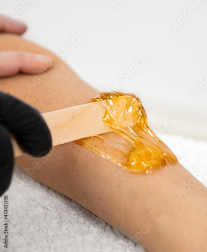 Hair removal process on female leg with depilation. Beautician applying the wax stick on the beautiful female legs. Beauty salon. High quality photo