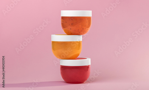 Set of round transparent glass jars with white plastic lids for cosmetics - body cream, oil, scrub, bath salt, gel, skin care, powder. Colorful pink background. High quality photo