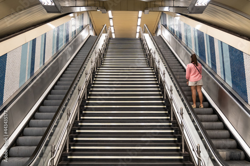 View of escalators with a staircase in the center in the subway and a woman on her back going up one of the escalators