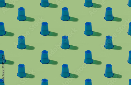 Plastic cups pattern. Utensils background. Waste management. Ecology problem. Set of blue symmetrical disposable empty glasses isolated on pastel green surface. photo