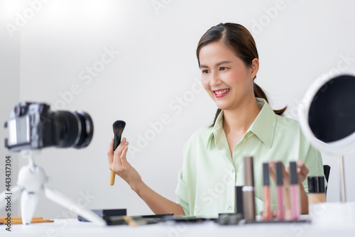 A beauty influencer applying powder blush on her cheek using makeup brush in front of a camera