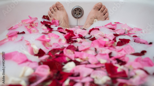 Funny picture of a man taking a relaxing bath. Close-up of male feet in a bath with foam and rose petals