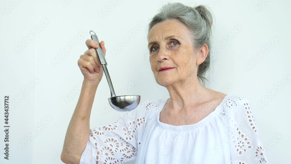 Emotional senior woman with silver hair is holding metal ladle or scoop on white background, happy retirement, mothers day concepts.