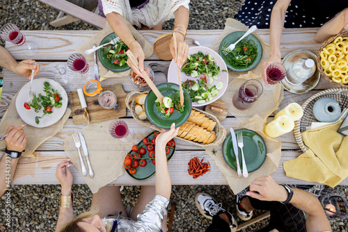 Group of people dining outdoors, view from above on the beautifully decorated wooden table with healthy food and drinks