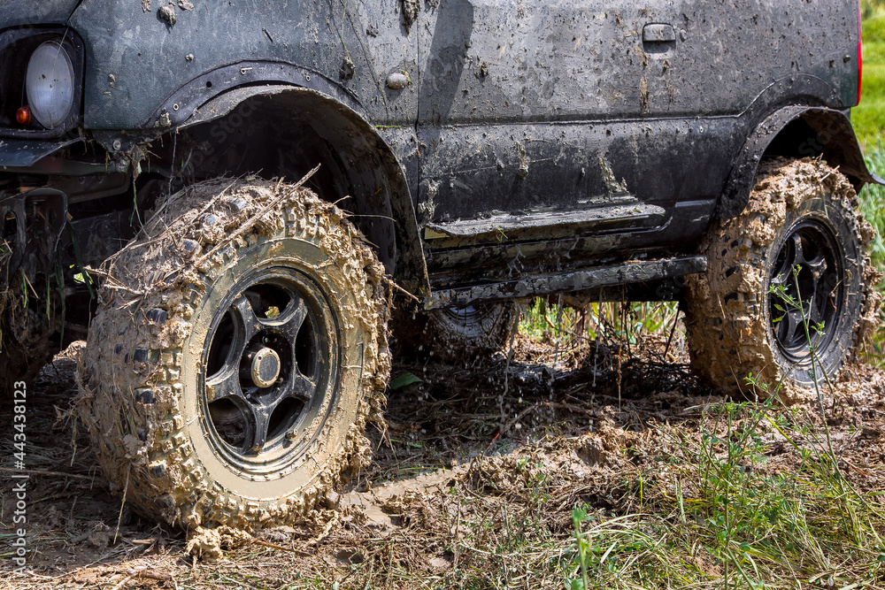 black SUV with big wheels dirty in a swamp stands on the grass, the water flows from the body after being flooded in the river, close-up side view, nobody. black SUV with big wheels dirty in a swamp stands on the grass, the water flows from the body after being flooded in the river, close-up side view, nobody.
