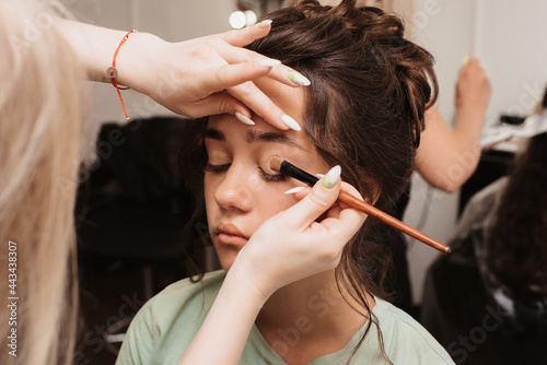 Shooting in a beauty salon. The makeup artist applies a shiny pigment to the eyes with a fluffy brush.