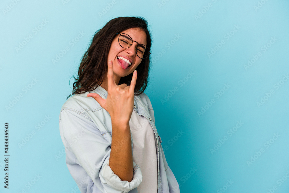Young caucasian woman isolated on blue background showing rock gesture with fingers Young caucasian woman isolated on blue background showing rock gesture with fingers