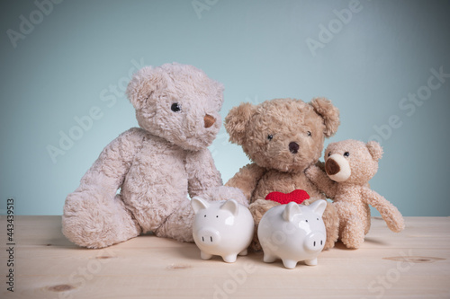 Concept banking, loan, save. Father, mother, and little bears with two white piggy banks on an old wooden table with copy space. Planning savings money to buy a home for a family to the future.