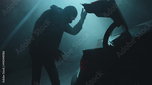 Handheld slowmo shot of young male criminal opening trunk of getaway car parked in dark garage He is looking into bag full of money and high-fiving his accomplice after successful robbery photo