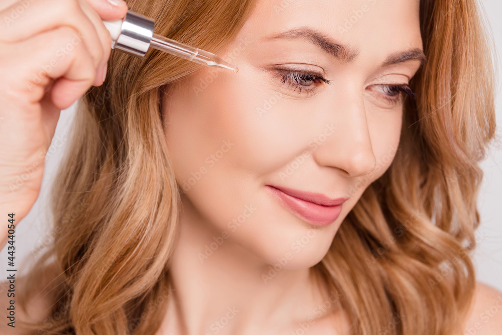 Cropped view portrait of attractive woman applying serum near eye lift effect isolated over grey pastel color background
