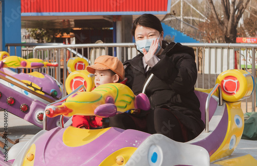 A young Chinese mother wearing a mask plays with her child in the playground