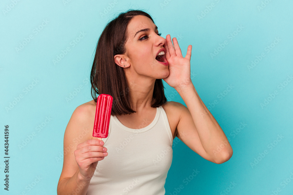 Young caucasian woman holding an ice cream isolated on blue background shouting and holding palm near opened mouth. Young caucasian woman holding an ice cream isolated on blue background shouting and holding palm near opened mouth.