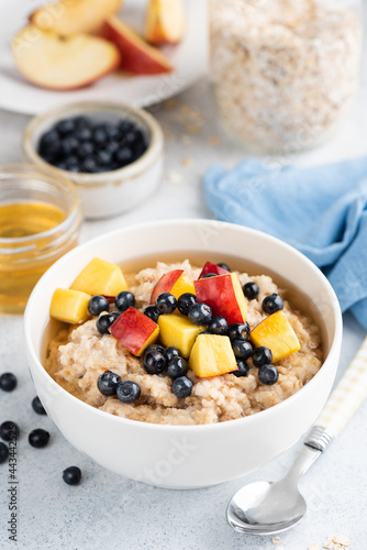 Oatmeal porridge with honey, peach cut in cubes and blueberries. Healthy vegetarian breakfast food