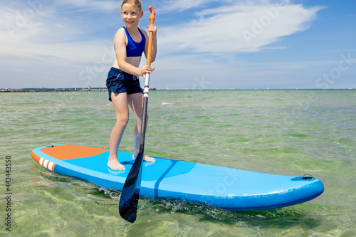 Cute little girl ecercise paddling on SUP board in sea on sunny day while summer holidays