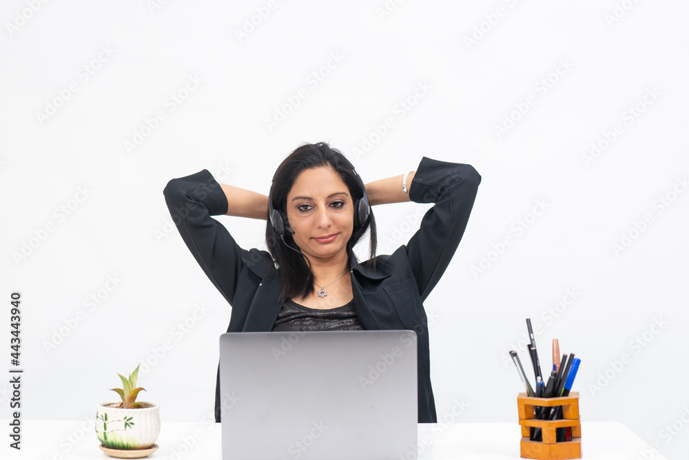 
Portrait of professional Indian businesswoman wearing headphones and working from her computer, Freelancer, work from home, Corporate lady, Hands behind head and relaxing.