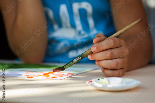 The child's hand draws a drawing with gouache paints.