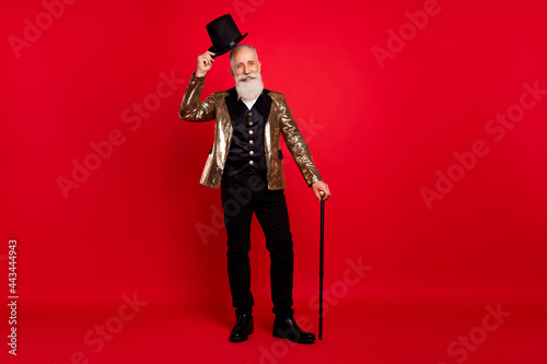 Full length photo of happy nice old man wear hat hold cane stick magician isolated on red color background