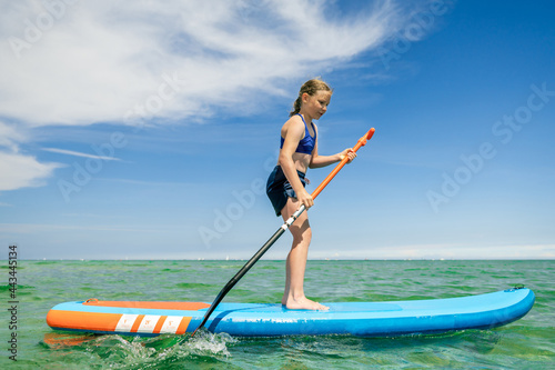 Cute little girl ecercise paddling on SUP board in sea on sunny day while summer holidays © spass