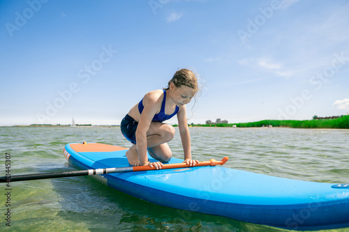 Cute little girl exercise to stay on paddle board in sea at sunny day while summer holidays