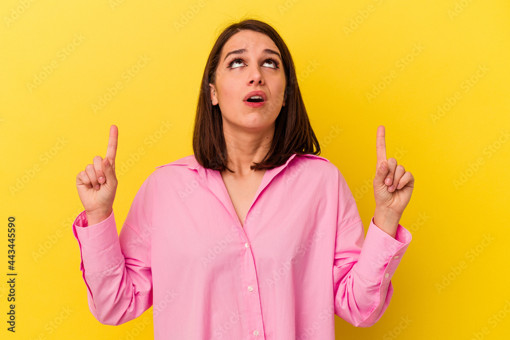 Young caucasian woman isolated on yellow background pointing upside with opened mouth. Young caucasian woman isolated on yellow background pointing upside with opened mouth.