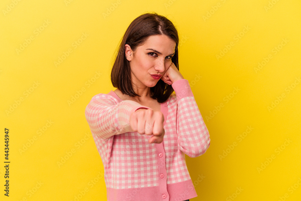 Young caucasian woman isolated on yellow background throwing a punch, anger, fighting due to an argument, boxing. Young caucasian woman isolated on yellow background throwing a punch, anger, fighting due to an argument, boxing.