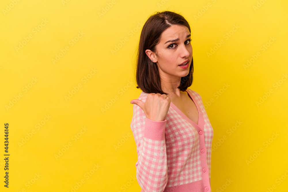 Young caucasian woman isolated on yellow background points with thumb finger away, laughing and carefree. Young caucasian woman isolated on yellow background points with thumb finger away, laughing and carefree.
