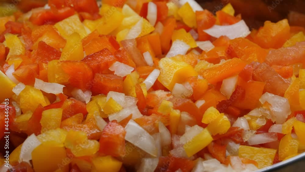 A vegatable close-up of fresh salsa with ingredients being added including red pepper, yellow pepper, orange pepper, onions, and tomatoes.