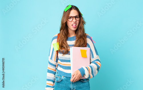 young pretty woman feeling disgusted and irritated and tongue out with a bag and holding books