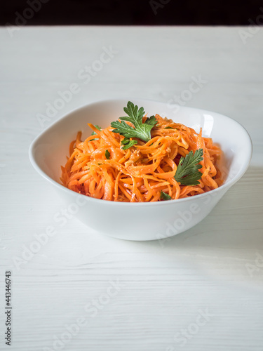 Spicy Asian salad with grated carrots and parsley. Korean carrots in a white bowl on a white background. Vegetarian diet. Healthy food concept. Vertical