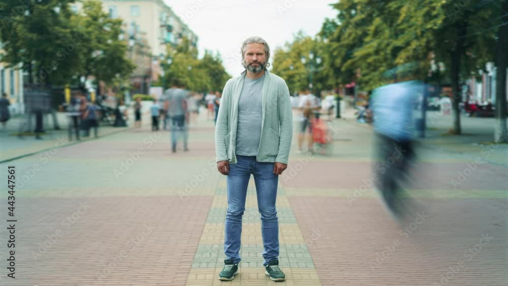 Time-lapse of handsome mature man standing in the street downtown and looking at camera with people walking around. Urban lifestyle and society concept.
