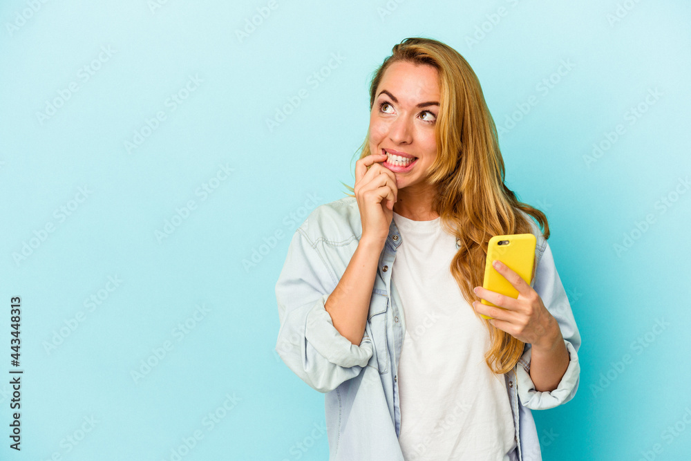 Caucasian woman holding mobile phone isolated on blue background relaxed thinking about something looking at a copy space. Caucasian woman holding mobile phone isolated on blue background relaxed thinking about something looking at a copy space.