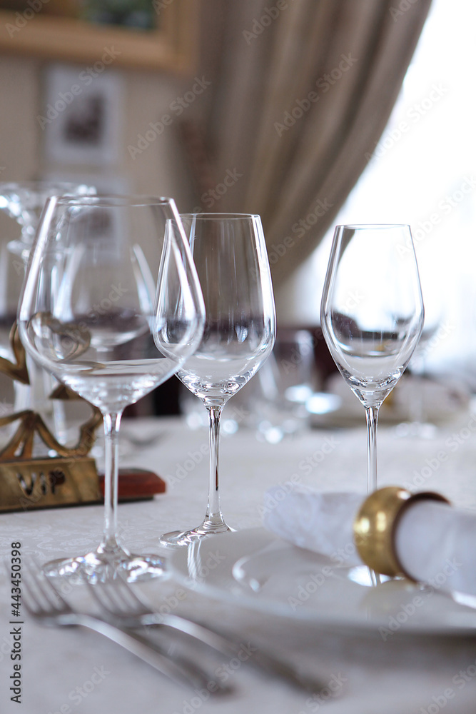 Festive table setting.Napkins made of cotton with brass rings. The concept of holidays.Wine glasses on the table. White plates. VIP lounge.White tablecloth with a textured pattern. Out of focus. Festive table setting.Napkins made of cotton with brass rings. The concept of holidays.Wine glasses on the table. White plates. VIP lounge.White tablecloth with a textured pattern. Out of focus.