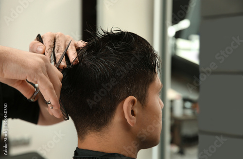 Professional barber making stylish haircut in salon, closeup