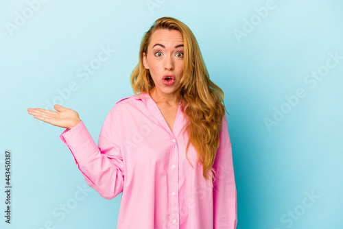 Caucasian woman isolated on blue background impressed holding copy space on palm.