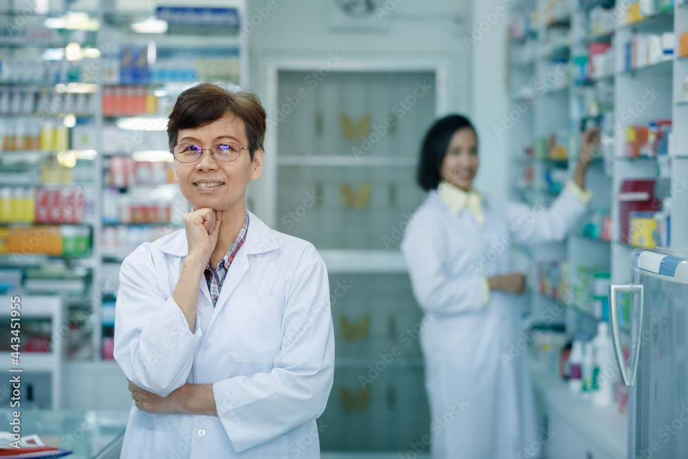 female pharmacist standing back couunter with hand on chin in pharmacy