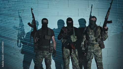 Portrait dolly-in shot of three armed terrorists in balaclavas posing for camera in their hideout photo
