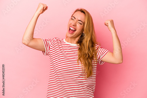 Caucasian blonde woman isolated on pink background raising fist after a victory, winner concept.