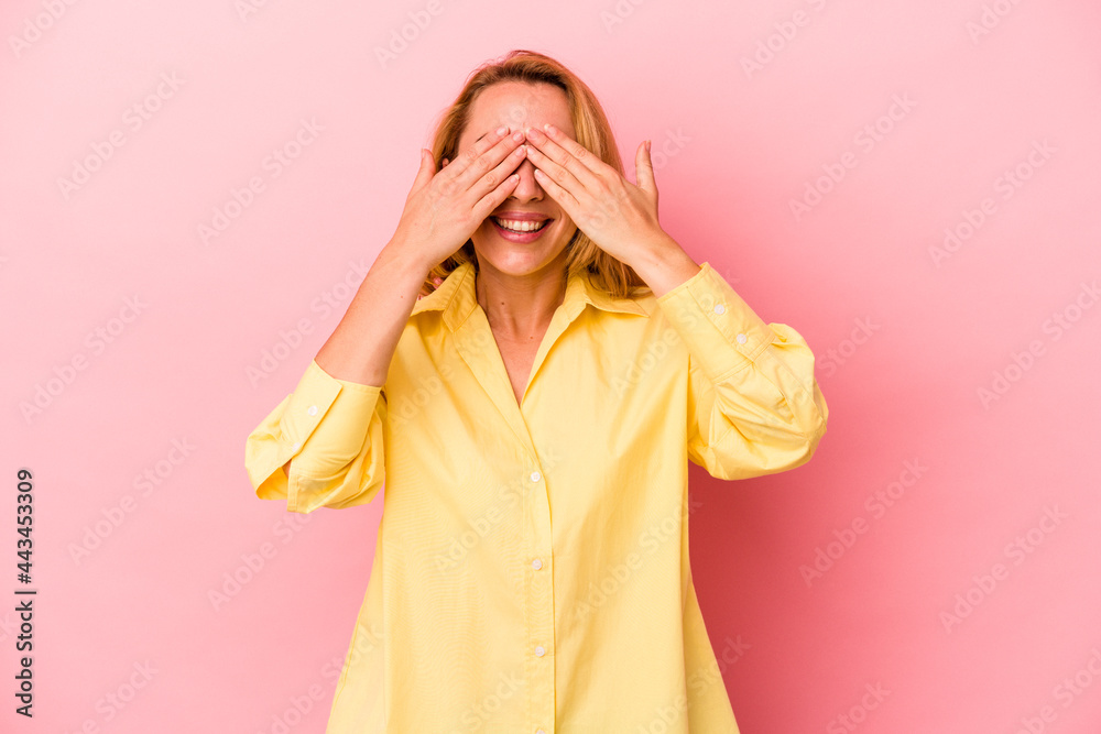 Caucasian blonde woman isolated on pink background covers eyes with hands, smiles broadly waiting for a surprise. Caucasian blonde woman isolated on pink background covers eyes with hands, smiles broadly waiting for a surprise.