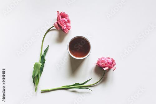 A cup of tea on a white background with pink tulips. Creative concept, flat lay, top view