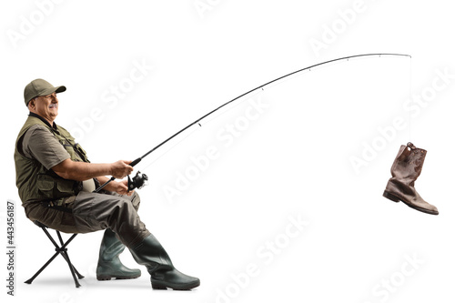 Obraz na plátně Mature fisherman sitting on a chair with a fishing rod and an old boot on the ho