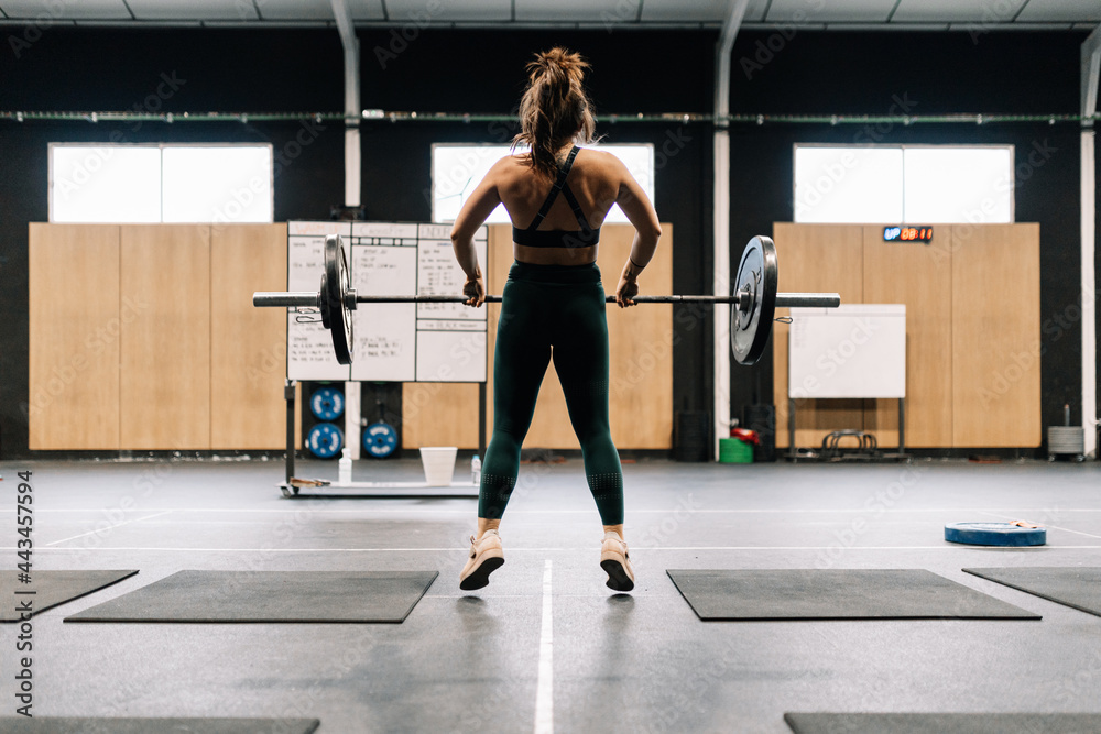 Obraz premium Young fitness woman doing barbell squats in a gym