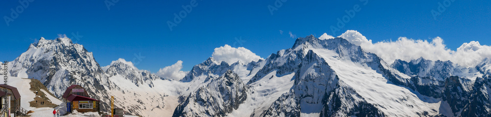 Panoramic view from Mount Mussa-Achitara to the Caucasian mountain range. Beautiful high snow-capped mountains with pointed peaks against the blue sky. Dombai, Karachay-Cherkess Republic, Russia