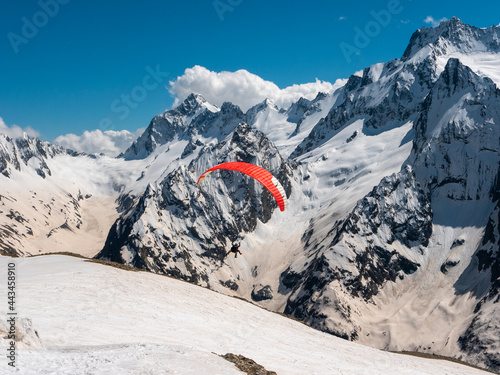 View from Mount Mussa-Achitara to the Caucasian mountain range. People are paragliding against the background of high snow-capped mountains and the blue sky. Dombai, Karachay-Cherkess Republic, Russia © lexosn