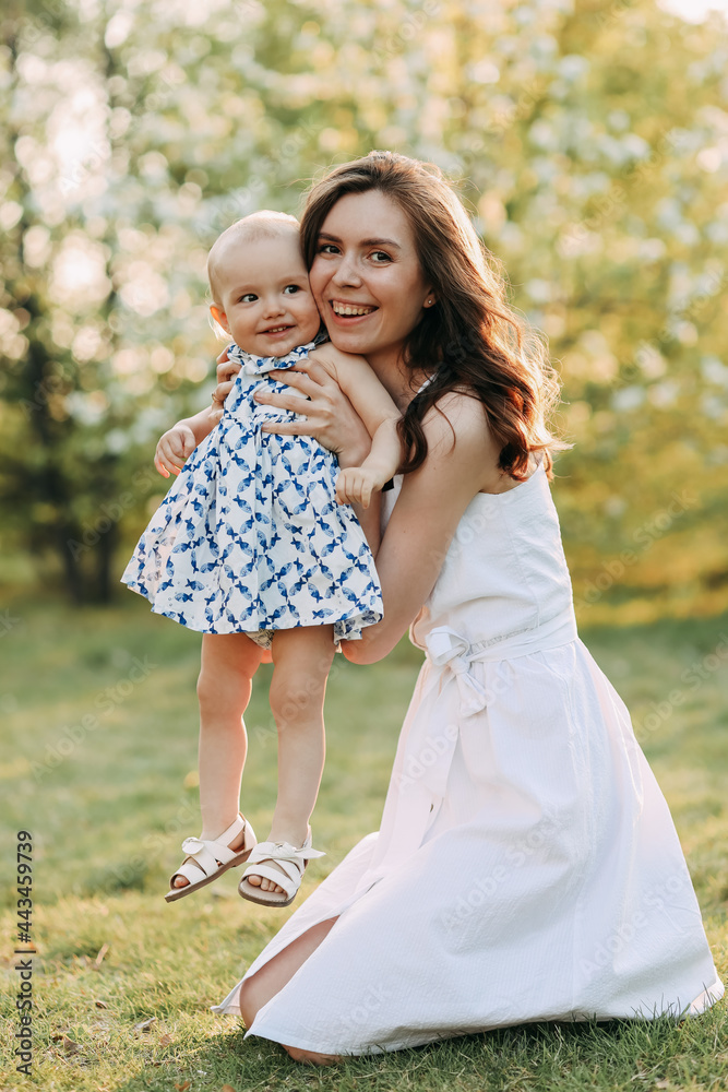 Happy loving cheerful mother and little daughter in summer clothes spend time together walking having fun smiling on a weekend in the blooming outdoor park Happy loving cheerful mother and little daughter in summer clothes spend time together walking having fun smiling on a weekend in the blooming outdoor park