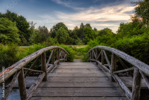 Wooden Bridge over the pond on a walking path in a famous Stanley Park. Sunset Summer Sky. Downtown Vancouver, British Columbia, Canada.