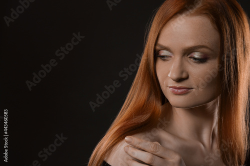 Portrait of happy young woman with charming smile and gorgeous red hair on dark background, space for text