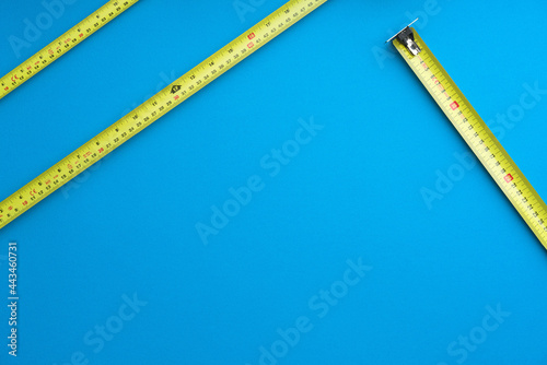 Yellow tape measures on solid coloured blue background