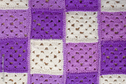 Woolen, knitted blanket. Consists of multi-colored squares knitted with woolen threads. The squares are purple, purple, white and sewn together. Textured image for the background. Front view.