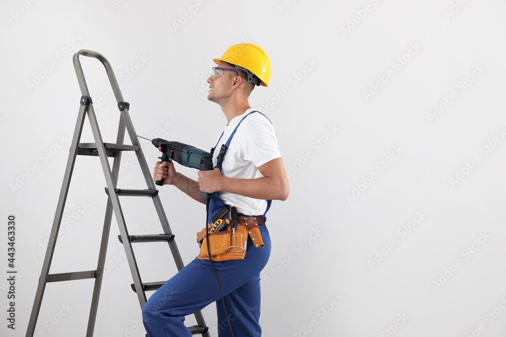 Worker with electric drill on ladder indoors, space for text Worker with electric drill on ladder indoors, space for text